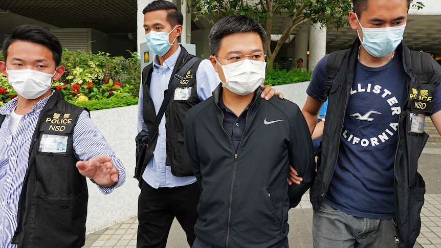 Ryan law being walked out of the Apple Daily office with arms behind his back escorted by the police officers.