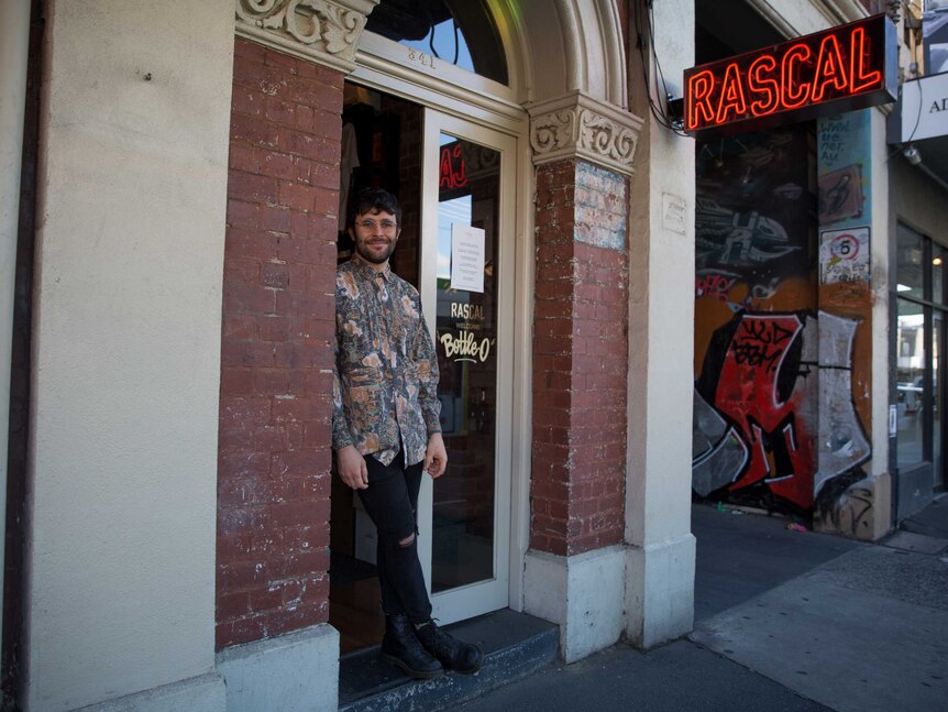 Harrison stands in the door of their brick building under a red neon Rascal sign