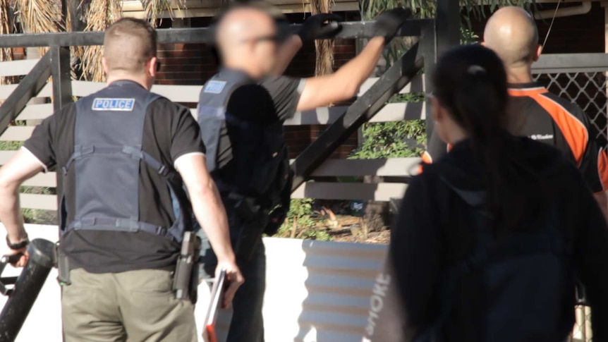 Detectives approach the fence of a property in Kalgoorlie during a drug raid.