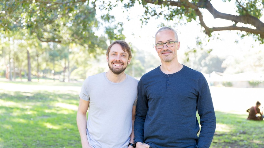 Two men stand side-by-side in a park