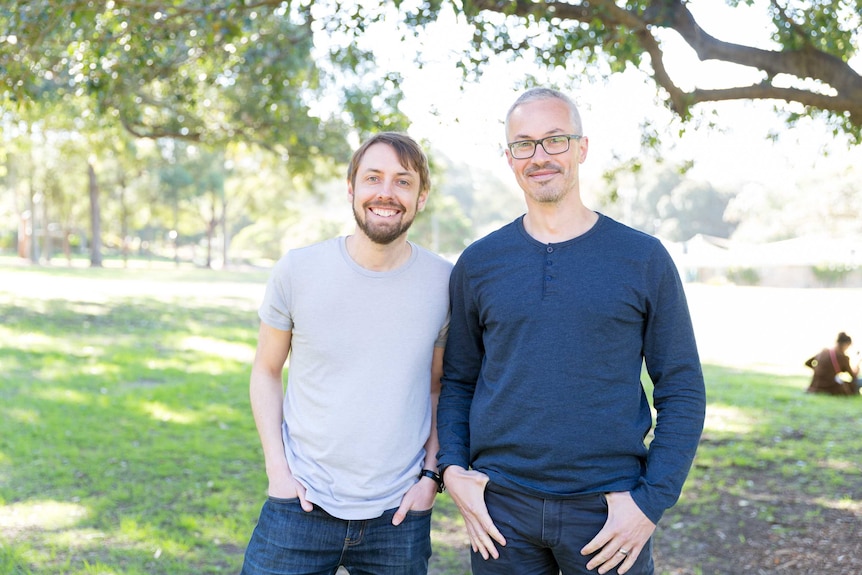 Two men stand side-by-side in a park