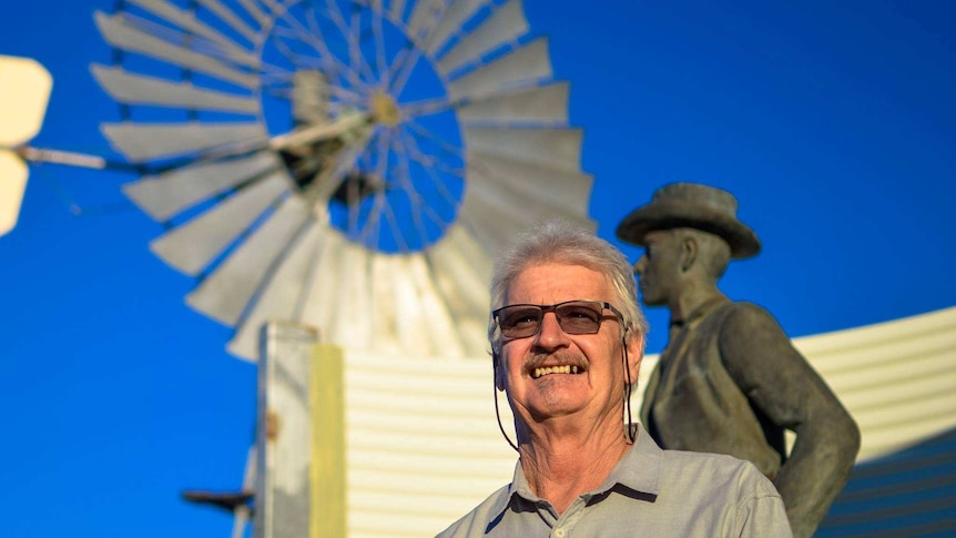 Butch Lenton smiling in the afternoon light, standing out the front of a windmill and blue sky.