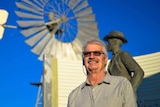 Butch Lenton smiling in the afternoon light, standing out the front of a windmill and blue sky.