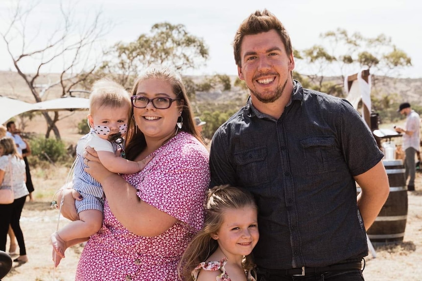 A family picture of a woman holding a male toddler and her husband and 7-year-old daughter