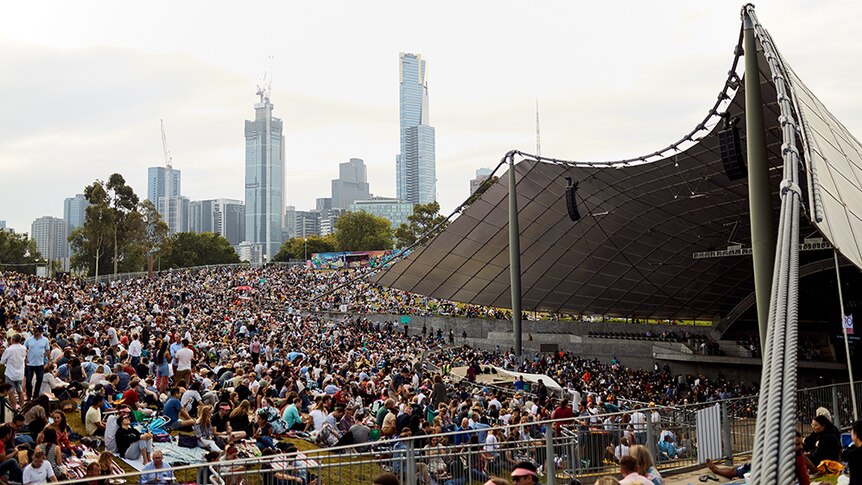 A large crowd of people sit outside and open-air stage at Melbourne's Myer Music Bowl.