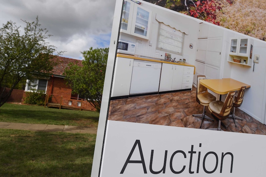 Auction sign in front of house with lawn and footpath