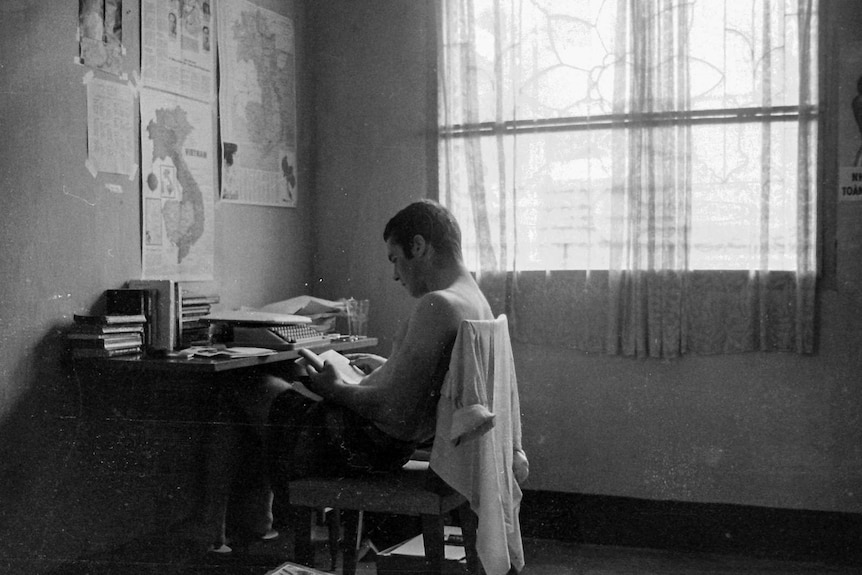 Derek Maitland sitting at a desk reading a book.