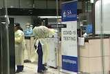 People wearing protective clothing behind a glass wall with a sign saying SA Pathology