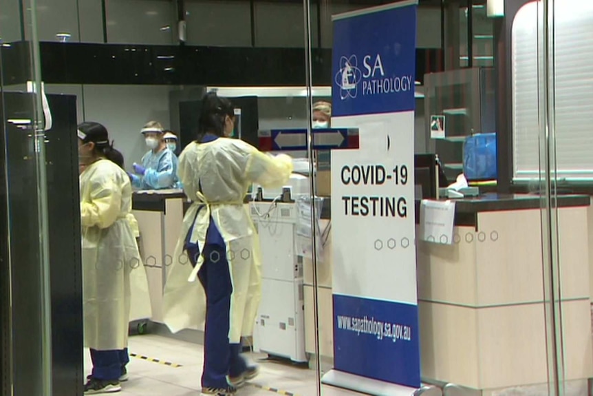 People wearing protective clothing behind a glass wall with a sign saying SA Pathology