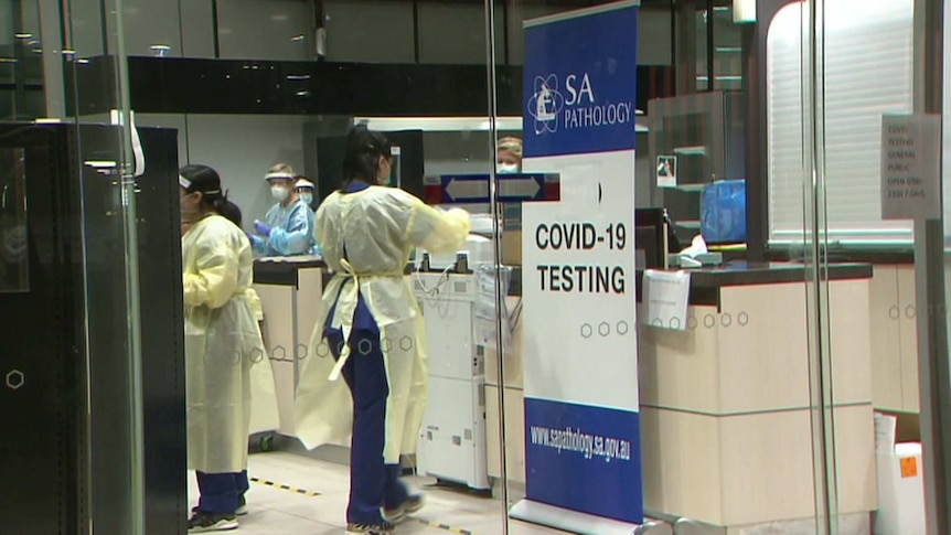 People wearing protective clothing behind a glass wall with a sign saying SA Pathology